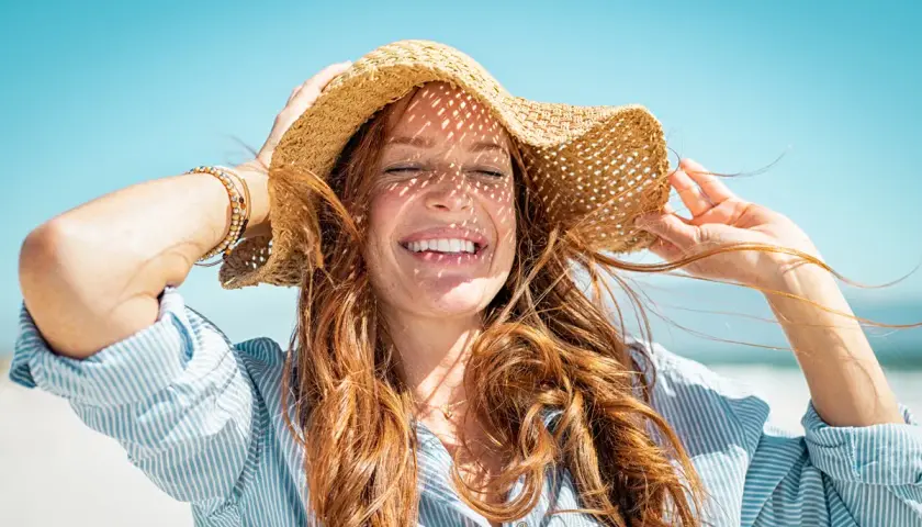 Mujer sonríe bajo sombrero de paja, con el pelo suelto. Consejos para como cuidar el pelo en verano.