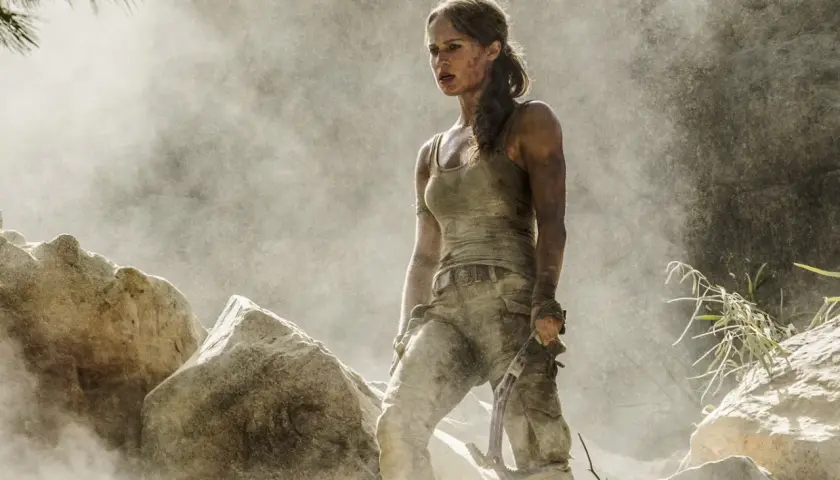 Alicia Vikander jako Lara Croft, wspinająca się po skalistym terenie, otoczona pyłem i mgłą.