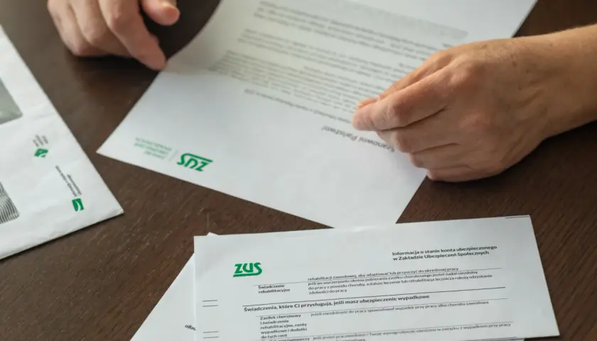 Dłonie przeglądają dokumenty ZUS. Informacje o świadczeniach i tym, jak przejść na emeryturę, są kluczowe.