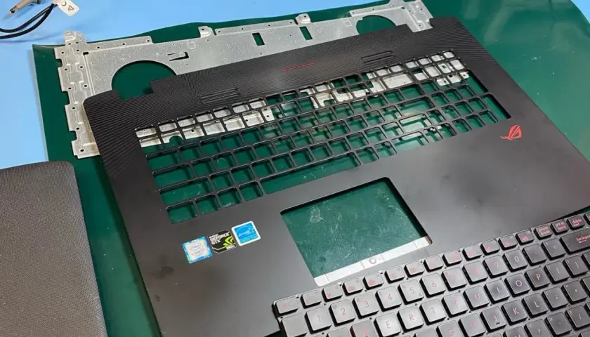 Części laptopa ROG gotowe do wymiany klawiatury. Widoczna górna obudowa z miejscem na klawisze i nowa klawiatura z czerwonymi oznaczeniami.