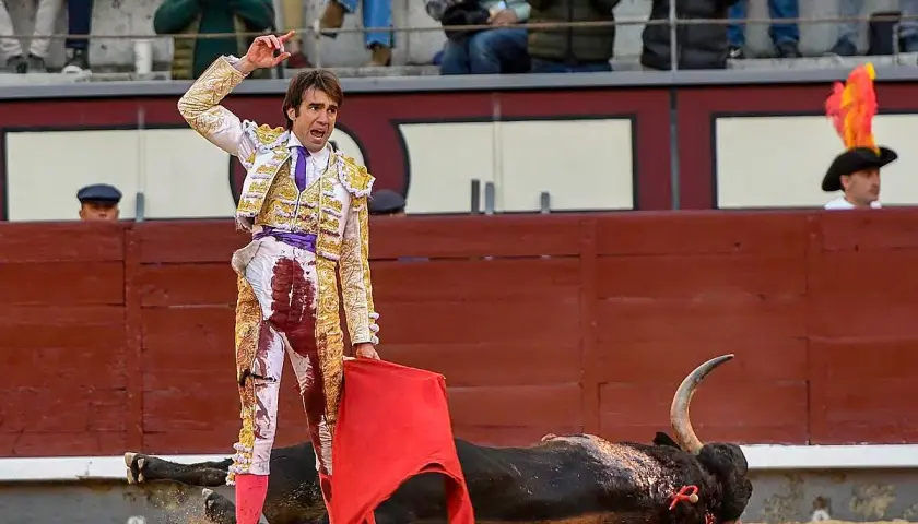 Un torero herido, con su traje manchado de sangre, se alza triunfante sobre un toro caído. La escena evoca la cruda realidad de la muerte torero.