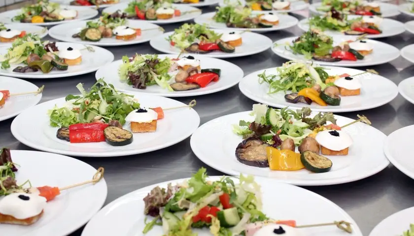 Organisation buffet : assiettes individuelles de salade fraîche, légumes grillés et amuse-bouches joliment dressés, prêts à être servis.