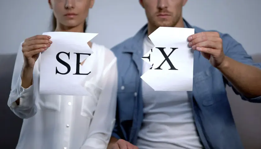 Coppia strappa fogli con lettere "SE" e "X", simboleggiando la fine di una relazione o un'assenza di intimità, forse legata al concetto di asessuale significato.