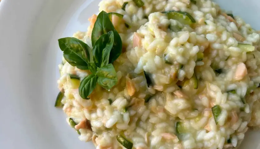 Un cremoso risotto con verdure, zucchine e pezzetti di salmone, guarnito con foglie di basilico fresco.