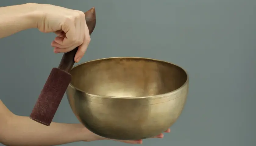 Dłonie trzymają mosiężną misę tybetańską i drewniany pucz.