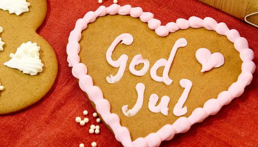 Hjärtformade pepparkakor med rosa glasyr och texten "God Jul". Bredvid syns en pepparkaka dekorerad med vita pepparkakor-liknande mönster.
