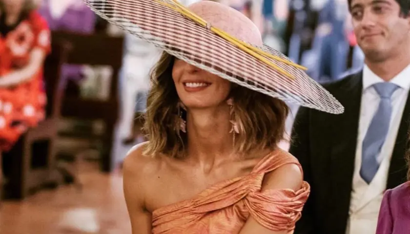 Peinado ondas invitada boda: mujer con sombrero de ala ancha y vestido naranja, sonriendo.