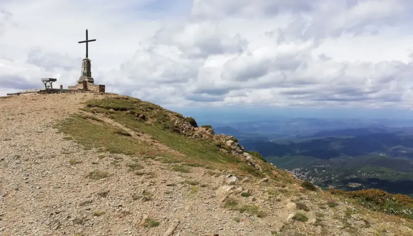 Cima de montaña con cruz y banco, ideal para **rutes per osona**. Paisaje de valles y nubes.