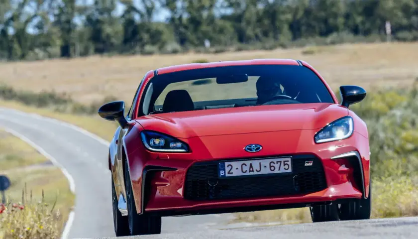 La Toyota sportiva rossa sfreccia su una strada tortuosa, con il sole che illumina il suo design aggressivo.