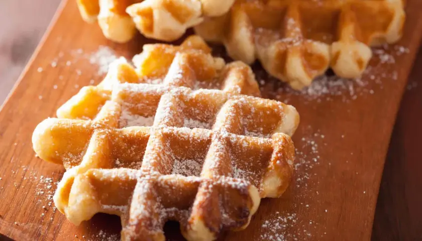 Gaufres liégeoises dorées saupoudrées de sucre glace sur une planche en bois. Un délice croustillant.