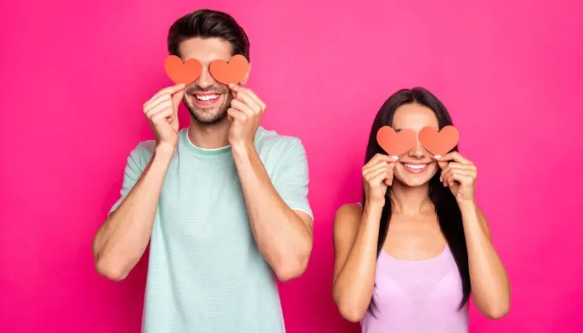 Coppia sorridente con cuori rossi sugli occhi, un modo giocoso per scoprire trucchi psicologici per capire se gli piaci.