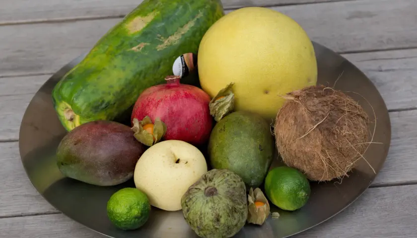 Talerz z owocami: papaja, mango, granat, pomelo, awokado, kokos, gruszka, limonki, custard apple i miechunka. Zastanawiasz się, czy można przewozić owoce w bagażu podręcznym?