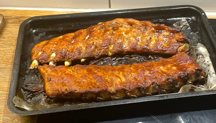 Två ugnsbakade kamben, glaserade och gyllene, ligger på en plåt. Doften av BBQ sprider sig i köket.