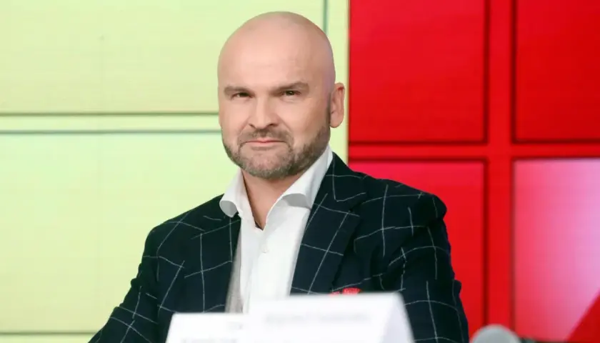 Rafał Brzoska, znany z budowania swojego majątku, w eleganckim garniturze siedzi przed ekranem.