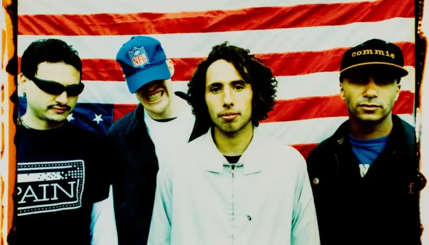 Członkowie Rage Against the Machine pozują przed amerykańską flagą. Jeden z nich ma na głowie czapkę z napisem "commie".