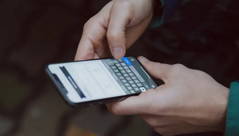 Dłonie trzymające smartfon z klawiaturą ekranową, jedna ręka naciska przycisk "Done".