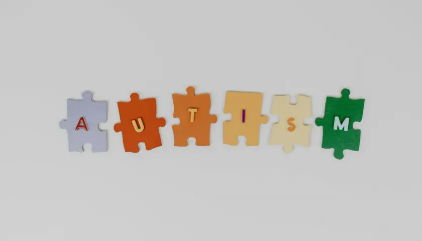Kolorowe puzzle układają się w napis AUTISM. Każdy element symbolizuje inny stopień niepełnosprawności w spektrum autyzmu.