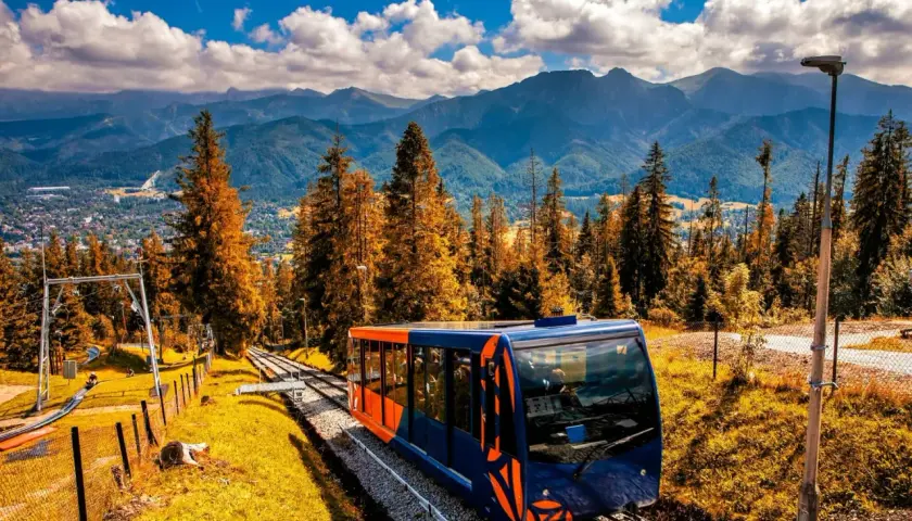 Kolejka linowa w Zakopanem pnie się wśród jesiennych drzew, oferując widok na Tatry.