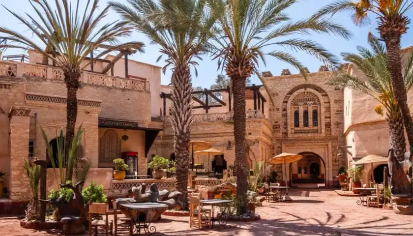 Sonniger Innenhof mit Palmen und traditioneller Architektur in der Agadir Altstadt. Tische und Stühle laden zum Verweilen ein.