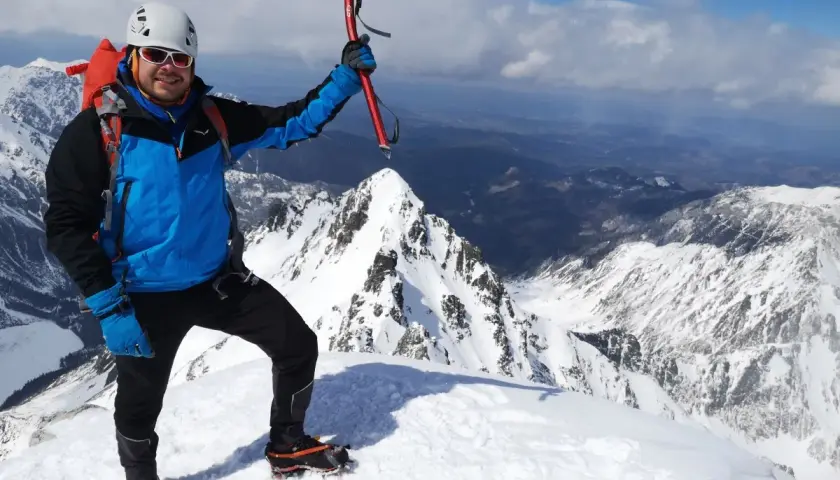 Szczęśliwy alpinista z czekanem na szczycie Rysów zimą. W tle rozległa panorama ośnieżonych gór.