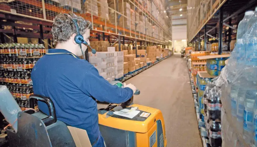 Mitarbeiter mit Headset führt Kommissionierauftrag per Sprachsteuerung (pick by voice) im Lager durch.
