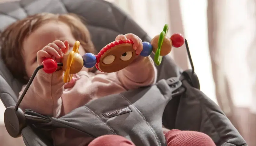 Maluch bawi się zabawką w leżaczku BabyBjorn. Od kiedy dziecko zaczyna sięgać po przedmioty, taki leżaczek jest idealny.