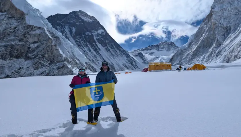 Polacy na Mount Everest dumnie prezentują flagę na tle majestatycznych gór. W tle widoczne namioty obozowe.
