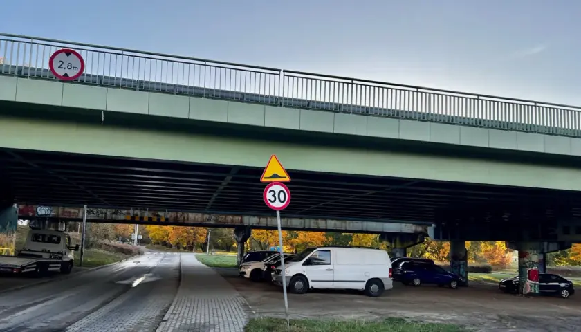 Pod estakadą zaparkowane są samochody. Widoczny znak ograniczenia wysokości 2,8m i znak ograniczenia prędkości do 30 km/h.