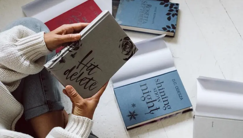 Une personne tient une jaquette de livre "Hit delete". D'autres livres sont disposés autour.