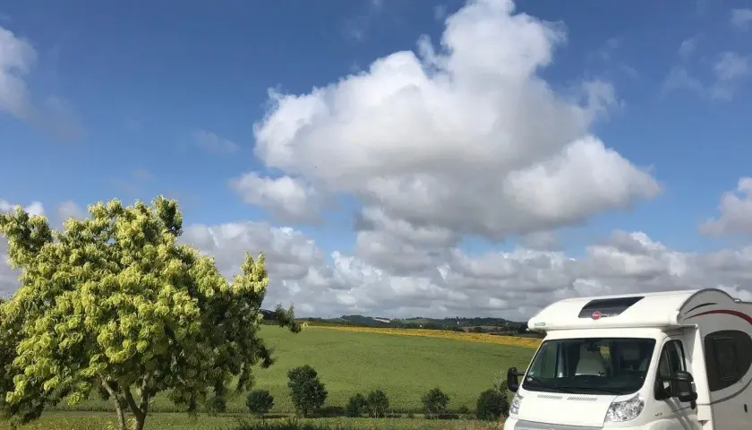 Camping-car en France, sous un ciel bleu et nuageux, avec un champ de tournesols en arrière-plan. La passion du voyage en camping-car.