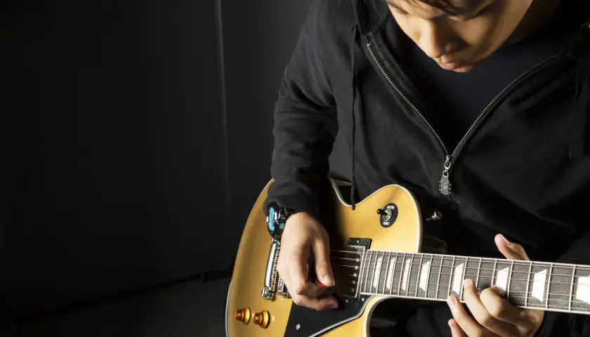 Młody muzyk ćwiczy, jak trzymać gitarę elektryczną. Złoty instrument i skupienie na grze.