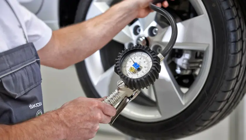 Mechanik sprawdza ciśnienie w oponie, używając manometru. To ważne, by wiedzieć, gdzie są czujniki ciśnienia w oponach i jak je kontrolować.