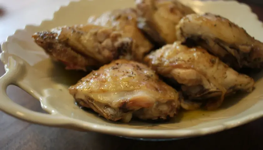 Plusieurs hauts de cuisse de poulet rôtis, assaisonnés d'herbes, reposent sur une assiette en céramique crème.