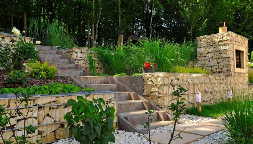 Moderne Gartenaufteilung Ideen mit Gabionenmauern, Steintreppen und üppiger Bepflanzung. Ein Kamin aus Steinen integriert sich harmonisch.