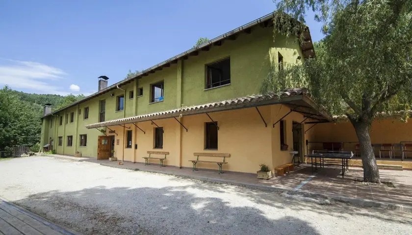 Edifici verd i groc amb taules de ping-pong i bancs a l'exterior. Un lloc ideal per a un refugi cap del rec.