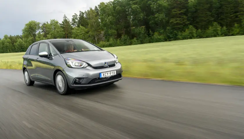 Grå Honda Jazz kör på en väg genom ett grönt landskap. Inga problem med denna bil, bara en härlig tur.