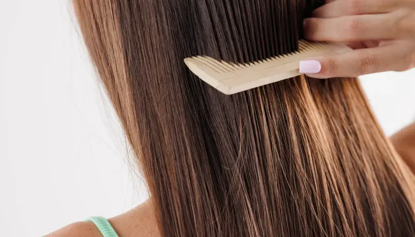 Peinando el pelo largo y castaño, que luce un poco apelmazado, con un peine de madera.