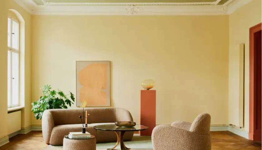 Ein Wohnzimmer mit gelben Wänden und einer grünen Decke, die frisch gestrichen wurde. Gemütliche Bouclé-Möbel und ein runder Couchtisch laden zum Verweilen ein.