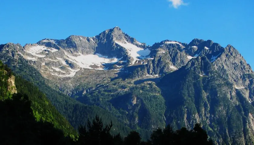 Majestuoso montarto pico nevado bajo un cielo azul. Bosques verdes cubren las laderas.