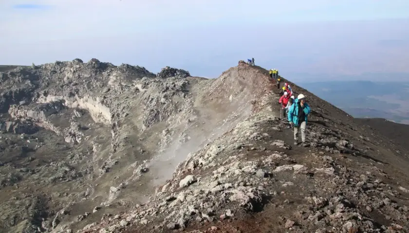 Escursionisti sul sentiero della cima Etna, tra rocce vulcaniche e fumo.