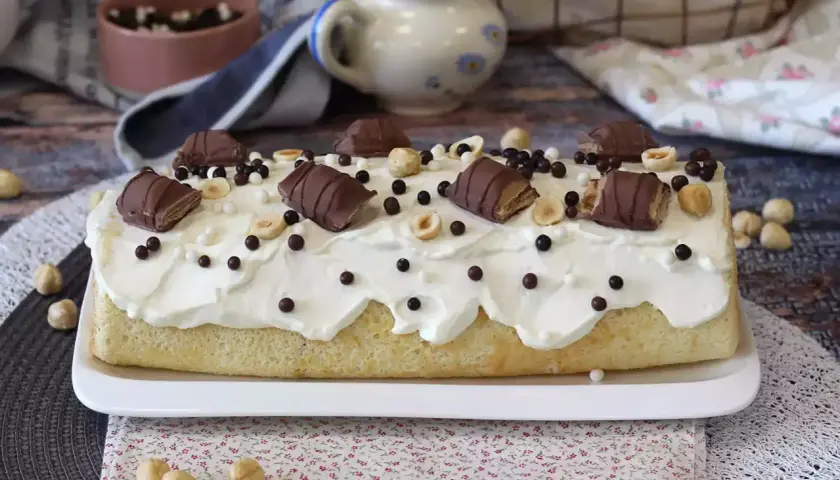 Puszysty biszkopt z kremem, udekorowany kawałkami batoników Kinder Bueno White, orzechami i czekoladowymi kuleczkami.