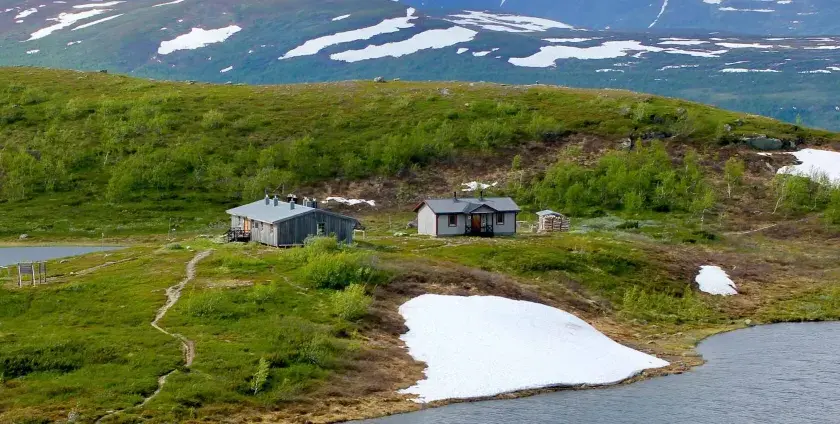 Fjällstugor längs Kungsleden nära Hemavan, med snöfläckar och gröna kullar.