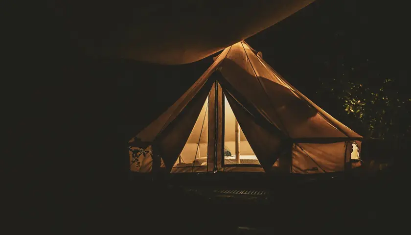 Nocne darmowe pola namiotowe. Oświetlony namiot tipi w ciemności, zapraszający do odpoczynku.