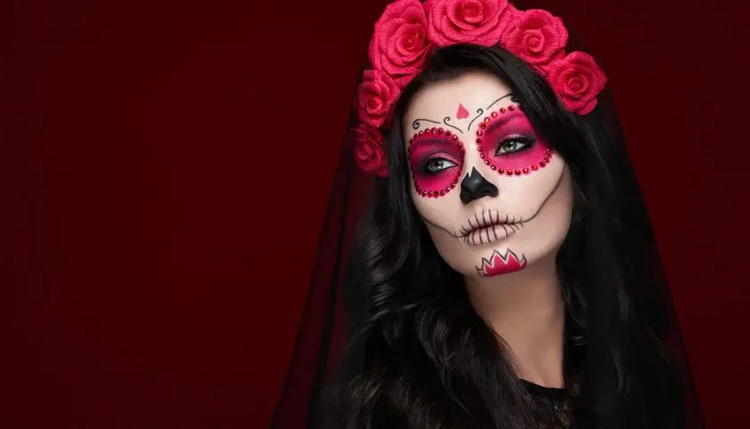 Kobieta z makijażem sugar skull, ozdobiona różami i welonem. Przerażające makijaże na Halloween w pełnej krasie.