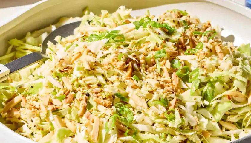 A refreshing Japanese cabbage recipe salad, topped with toasted almonds, sesame seeds, and green onions, served in a white bowl.