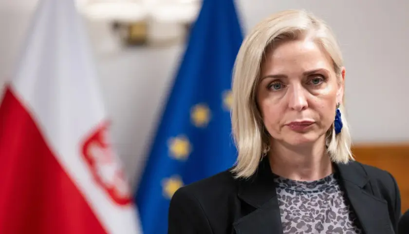 Znana posłanka KO zrezygnowała z mandatu dla kariery w biznesie prywatnym. Na zdjęciu kobieta z blond włosami, w czarnej marynarce, na tle flag Polski i UE.