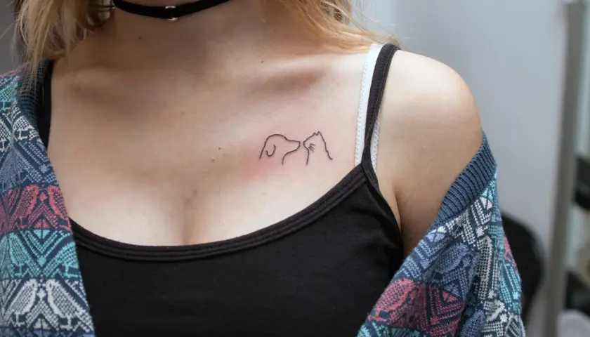 Minimalistyczny tatuaż pies i kot na dekolcie, symbol przyjaźni między gatunkami.