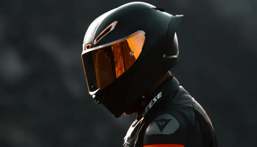 Casco da moto sportivo con visiera arancione riflettente, uno dei tanti tipi di casco per la sicurezza in pista.