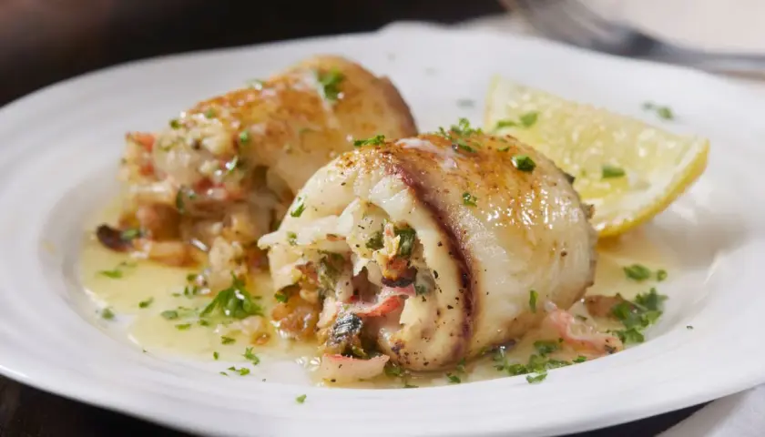 Involtini alla messinese ripieni di pesce e verdure, serviti su un piatto bianco con spicchio di limone e prezzemolo tritato.