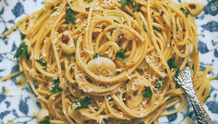 Pyszny makaron aglio olio z czosnkiem, natką pietruszki i płatkami chili, posypany parmezanem.